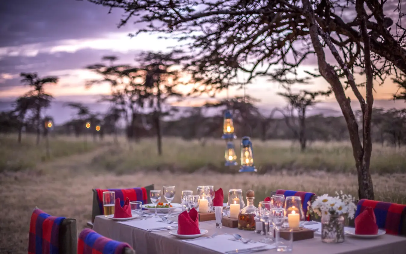 Outdoor dinner table set in savanna at dusk with lanterns, Sirikoi, Laikipia Highlands, Kenya