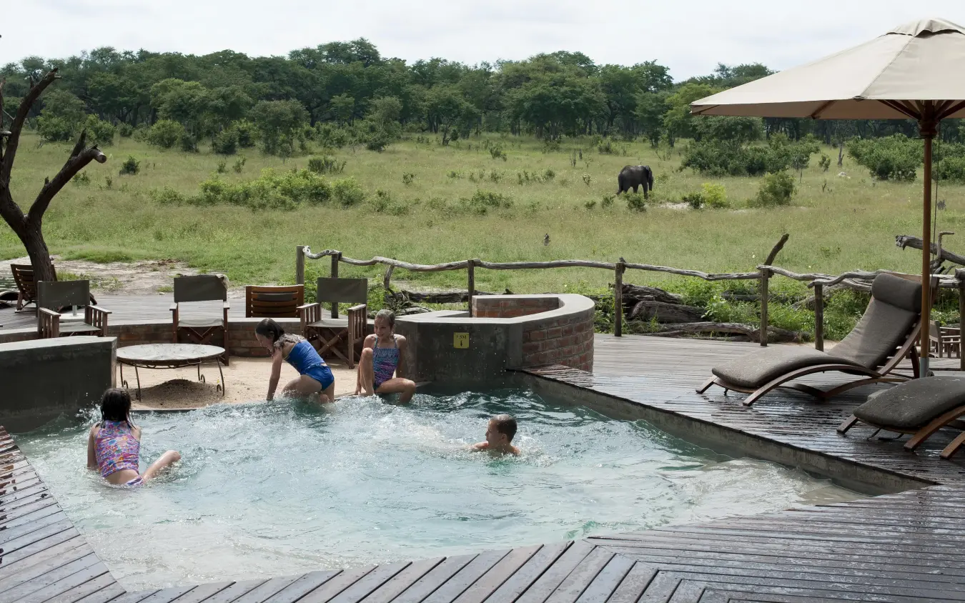 Family swimming in pool overlooking African savanna, Somalisa Acacia, Hwange National Park, Zimbabwe