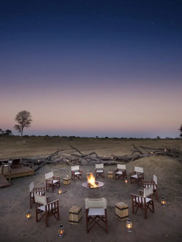 Outdoor dining setup with chairs and campfire under twilight sky, Somalisa Expeditions, Hwange National Park, Zimbabwe