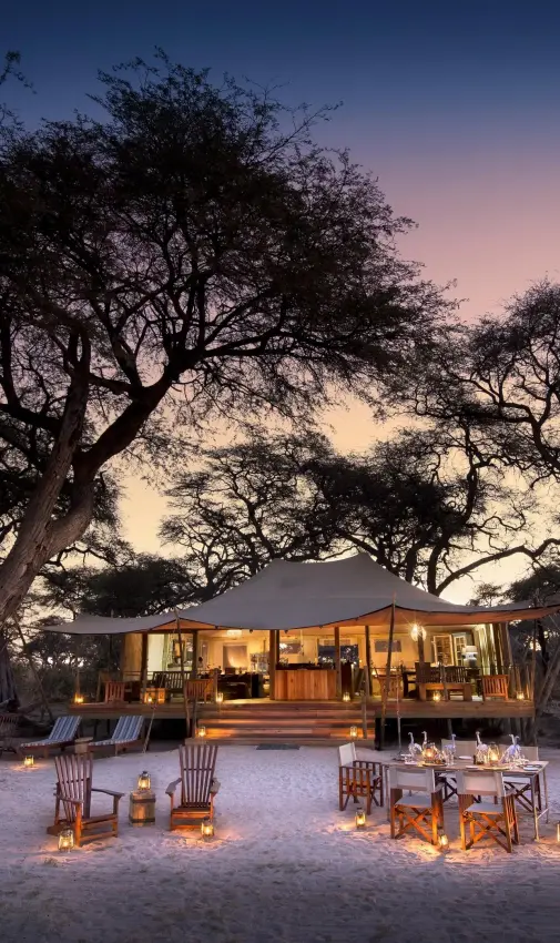 Canvas tent lodge at dusk with acacia trees and candlelit seating, Somalisa Expeditions, Hwange National Park, Zimbabwe