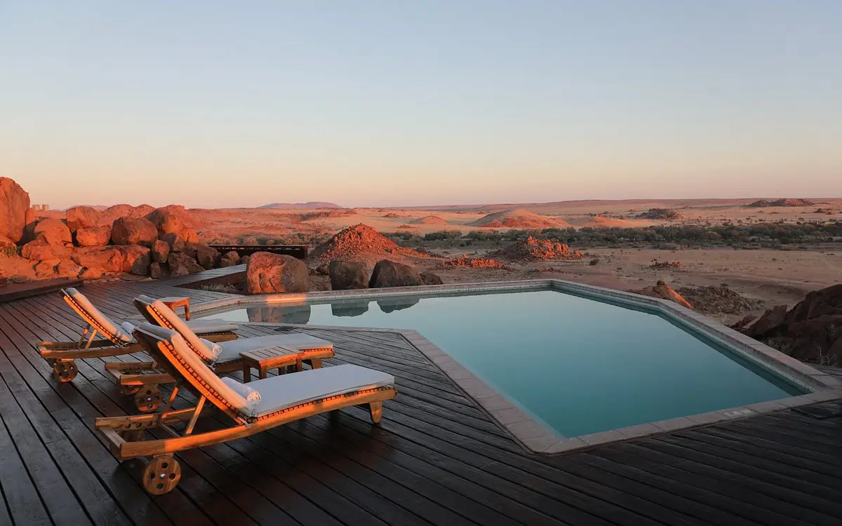 Infinity pool with lounge chairs overlooking desert landscape at sunset, Sorris Sorris, Damaraland, Namibia