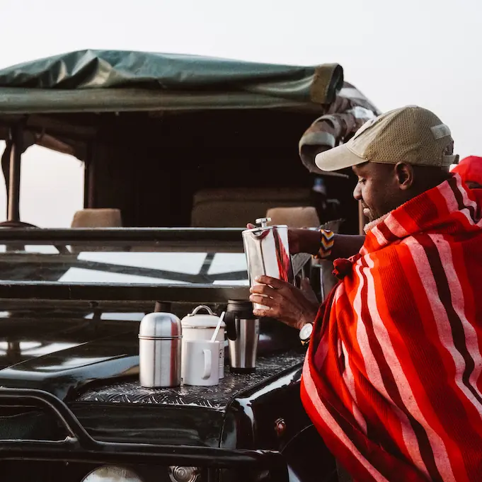 Guests wrapped in blankets on safari vehicle observing wildlife, Speke’s Camp, Maasai Mara, Kenya
