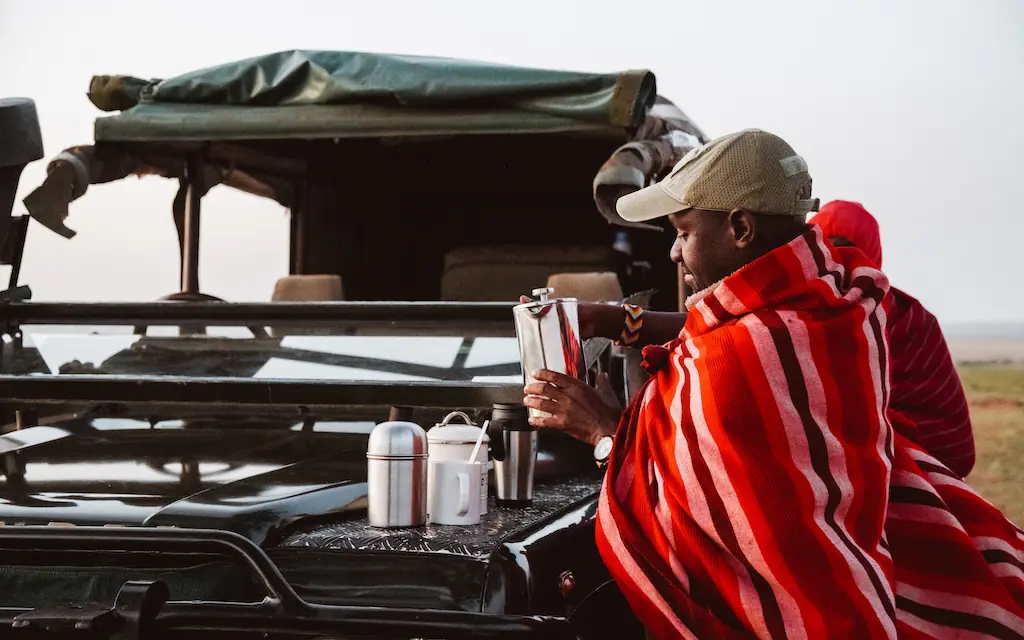 Guests wrapped in blankets on safari vehicle observing wildlife, Speke’s Camp, Maasai Mara, Kenya