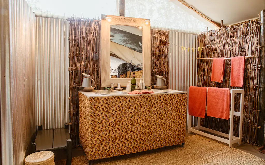 Bathroom vanity with mirror, woven details, orange towels, Speke’s Camp, Maasai Mara, Kenya