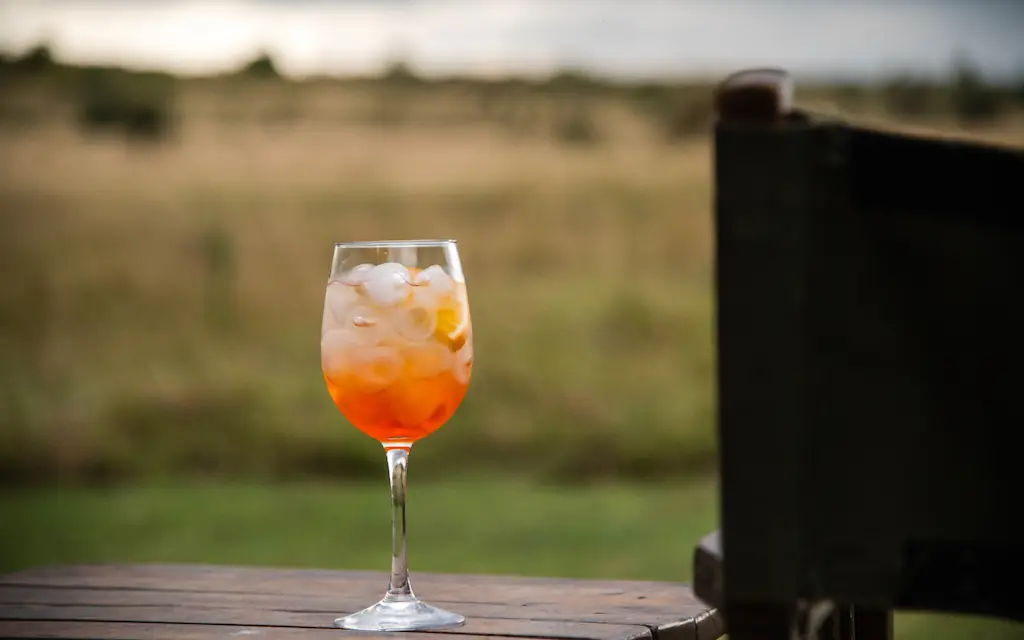 Aperitif cocktail on wooden deck overlooking savanna landscape, Speke’s Camp, Maasai Mara, Kenya
