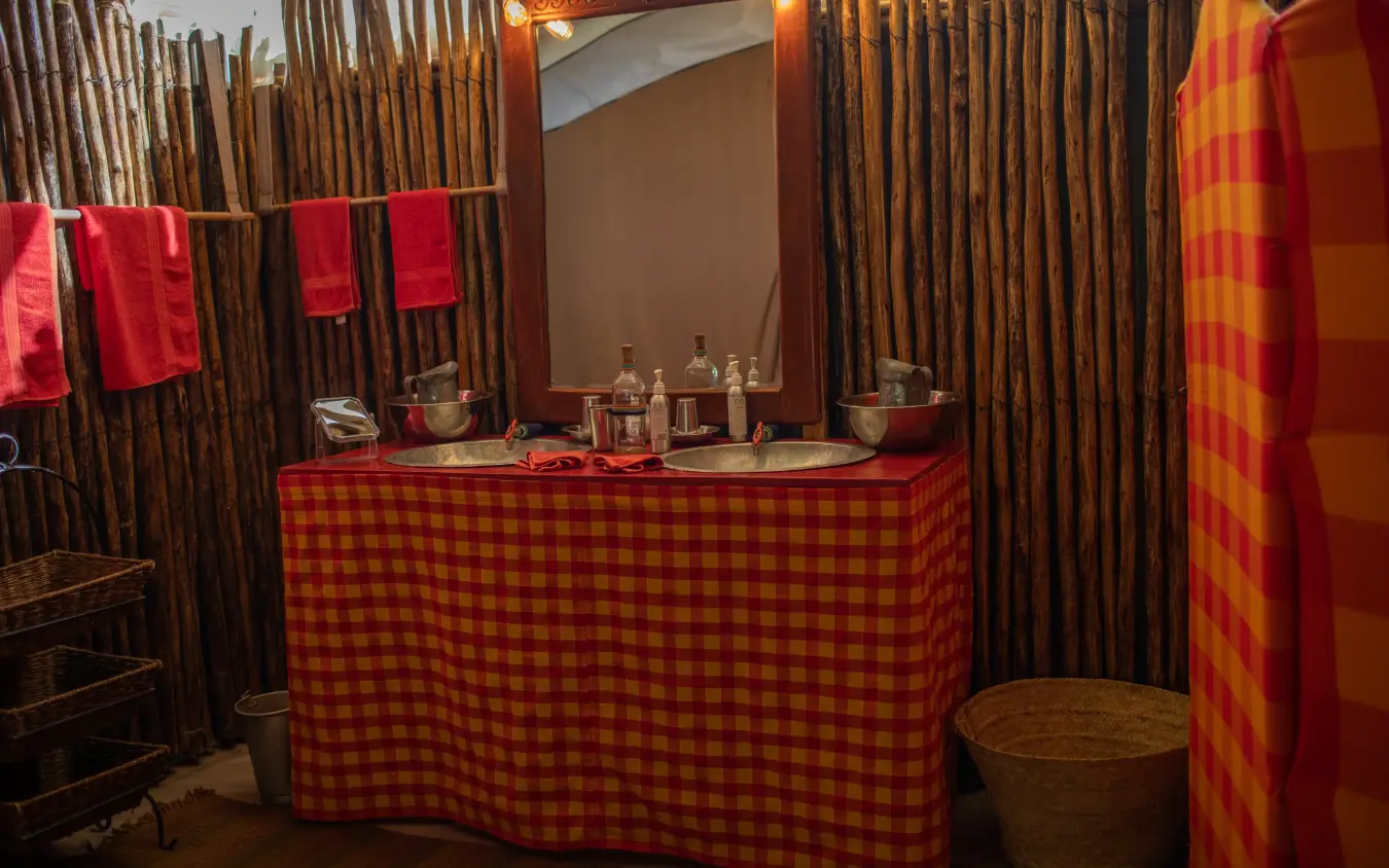 Rustic bathroom with red plaid fabric and wooden walls, Speke’s Camp, Maasai Mara, Kenya