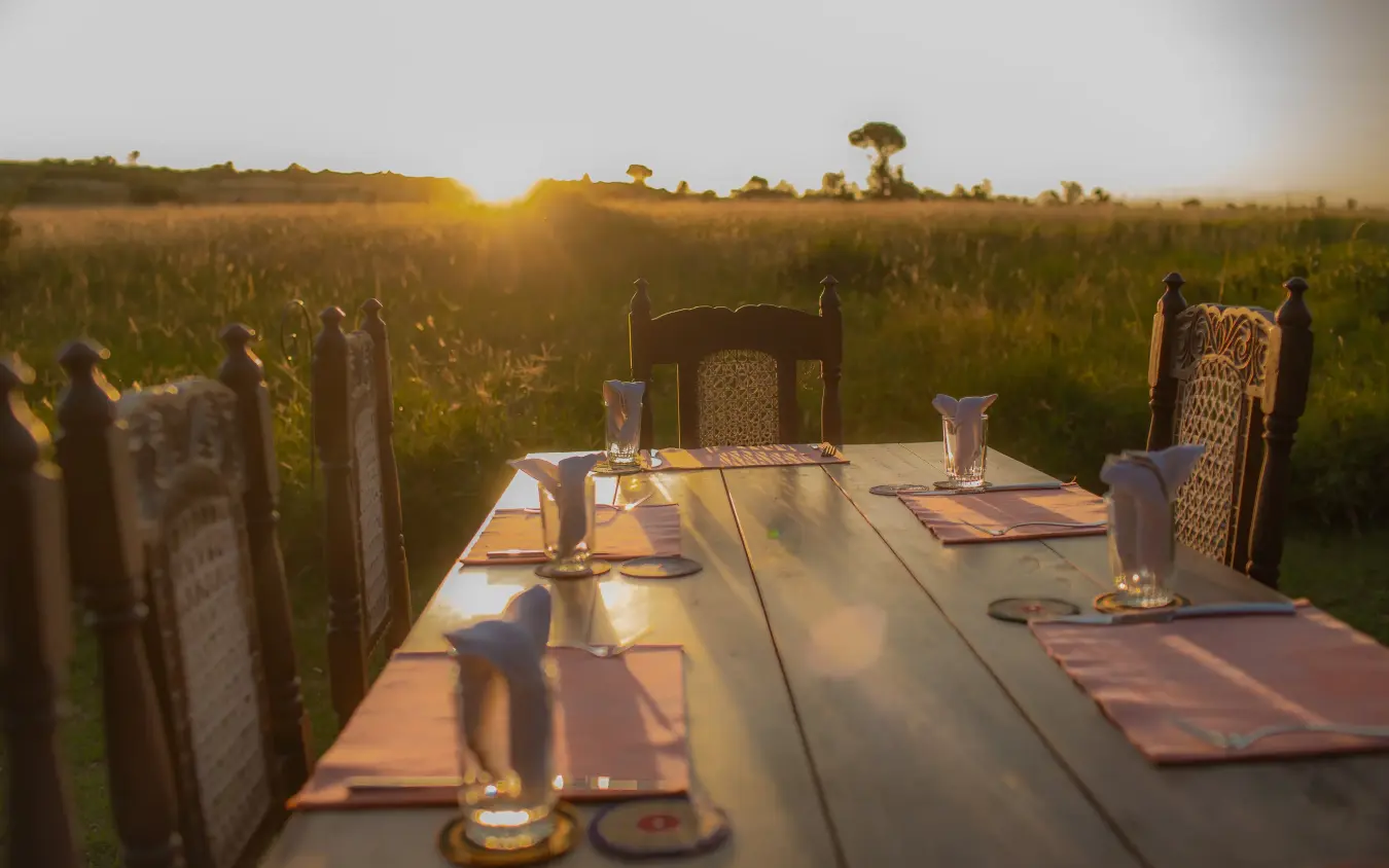 Dining table set in savanna grassland at sunset, Speke’s Camp, Maasai Mara, Kenya