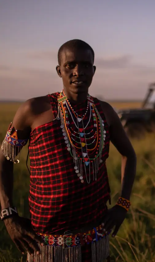 Maasai man in traditional red clothing on savanna, Speke’s Camp, Maasai Mara, Kenya