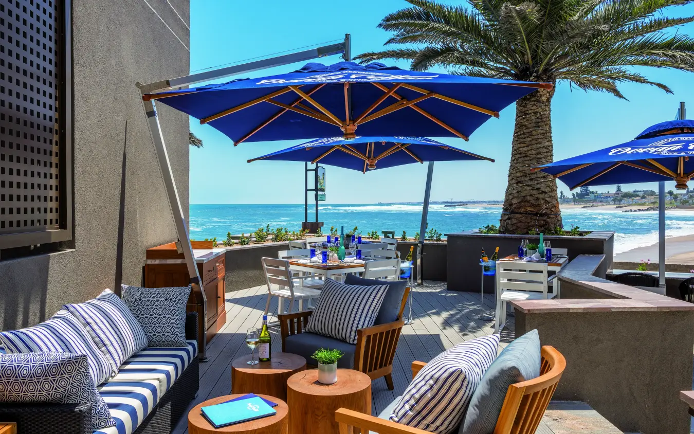 Beachfront dining terrace with blue umbrellas overlooking ocean, Strand Hotel Swakopmund, Swakopmund, Namibia