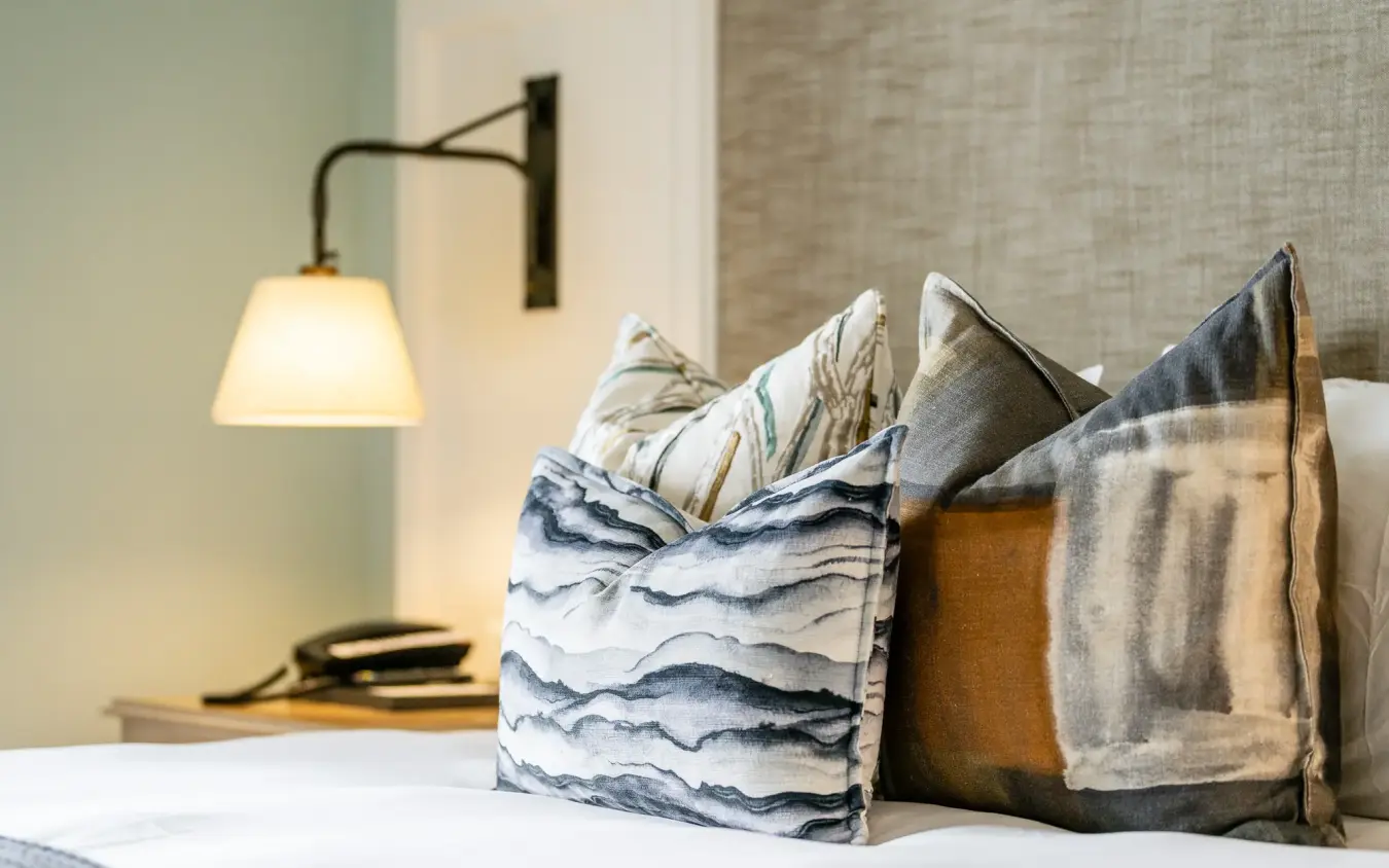 Bedroom bed with decorative pillows and wall-mounted reading lamp, Strand Hotel Swakopmund, Swakopmund, Namibia