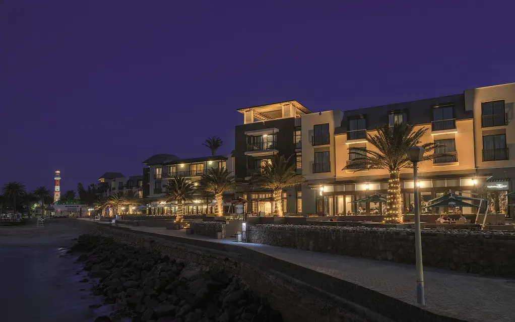 Waterfront luxury resort buildings illuminated at dusk with palm trees, Strand Hotel Swakopmund, Swakopmund, Namibia