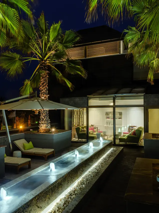 Modern villa terrace with illuminated water feature and palm trees at night, Strand Hotel Swakopmund, Swakopmund, Namibia