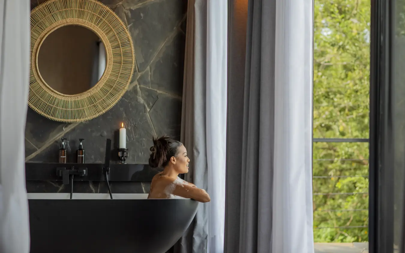Woman relaxing in black freestanding bathtub with garden view, Tarangire Elephant Springs, Tarangire National Park, Tanzania