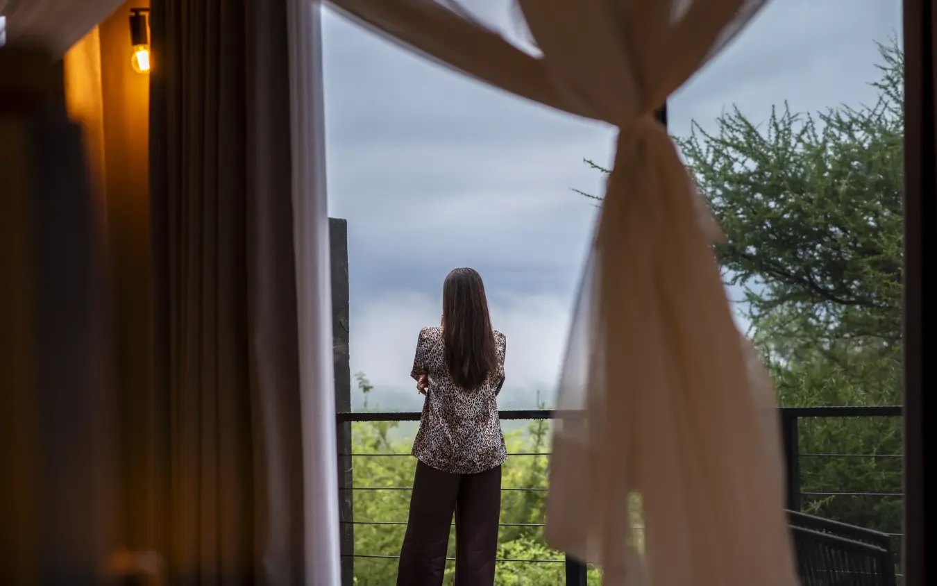 Woman standing on balcony overlooking green landscape at dusk, Tarangire Elephant Springs, Tarangire National Park, Tanzania