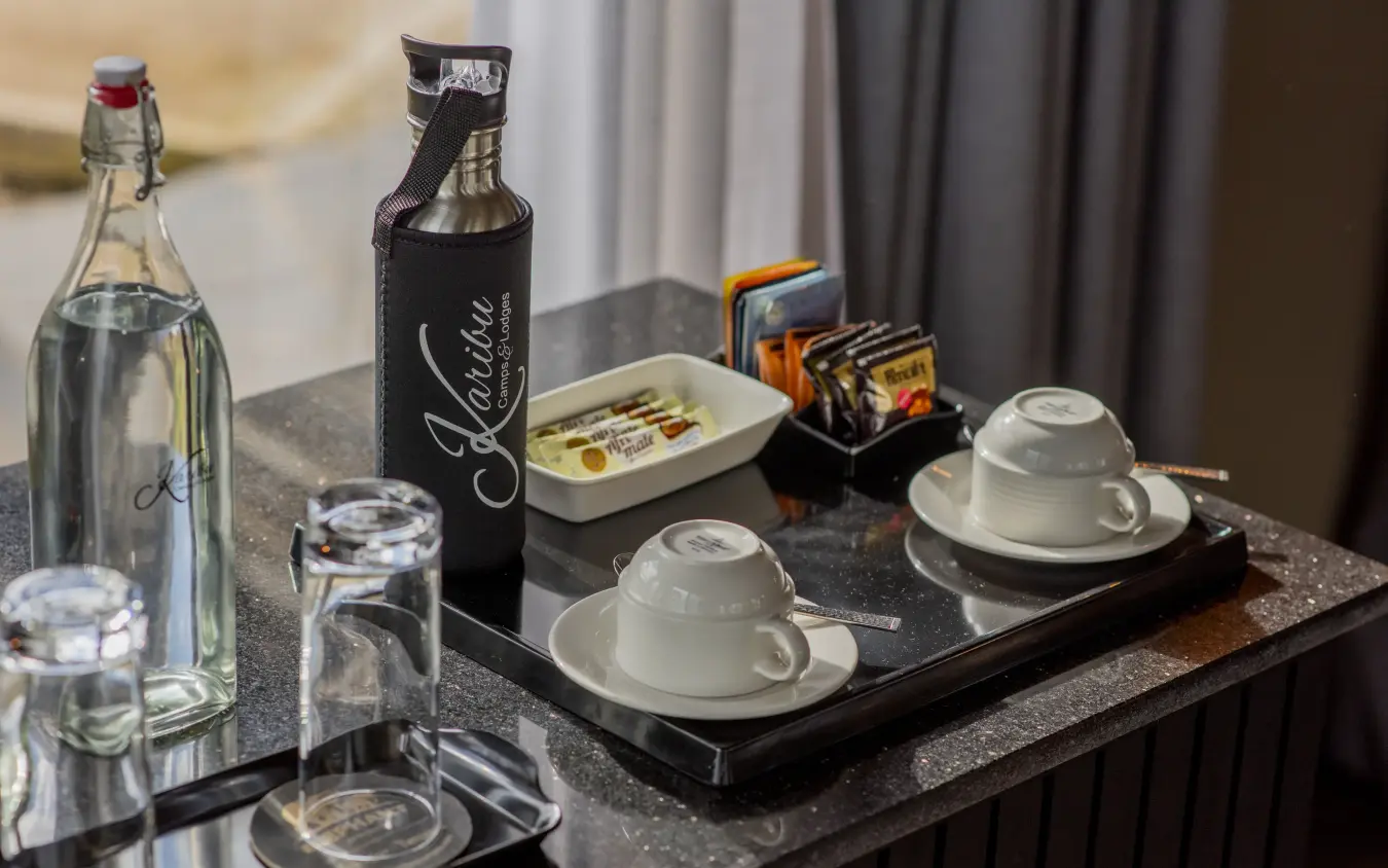 In-room welcome amenities with water bottles and coffee service on dark table, Tarangire Elephant Springs, Tarangire National Park, Tanzania
