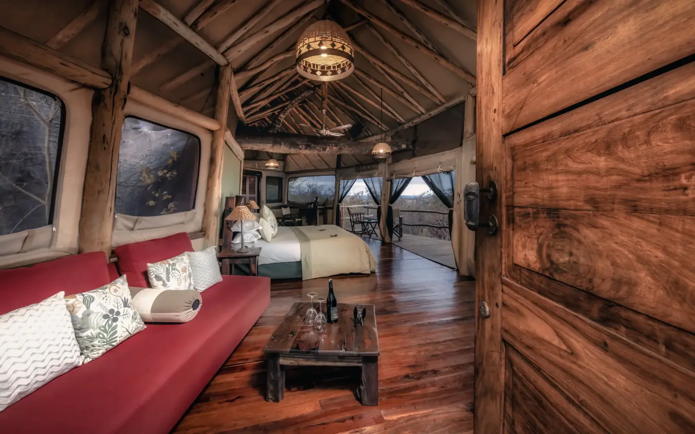 Luxury safari lodge interior with red sofa and wooden beam ceiling overlooking savanna, Tarangire Treetops, Tarangire National Park, Tanzania