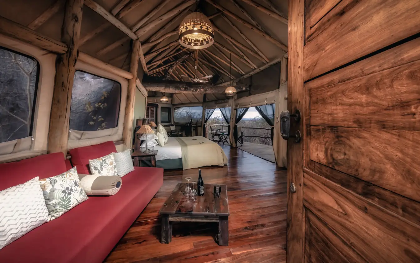 Luxury safari lodge interior with red sofa and wooden beamed ceiling overlooking savanna, Tarangire Treetops, Tarangire National Park, Tanzania