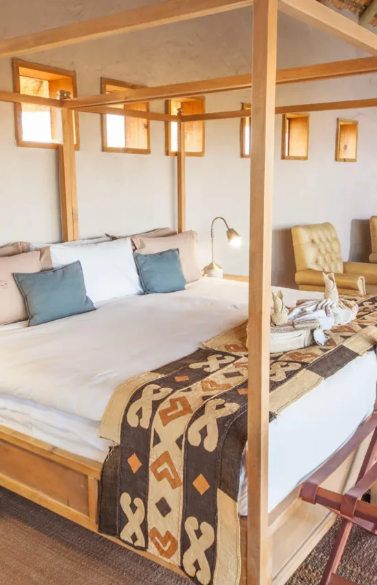 Spacious bedroom with wooden four-poster bed and seating area, Tau Pan Camp, Central Kalahari, Botswana