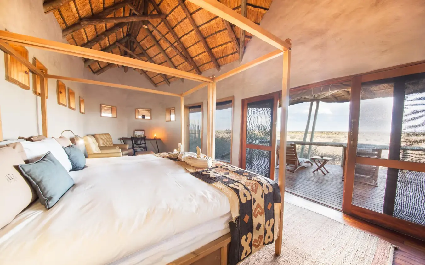 Spacious bedroom with four-poster bed and panoramic windows, Tau Pan Camp, Central Kalahari, Botswana