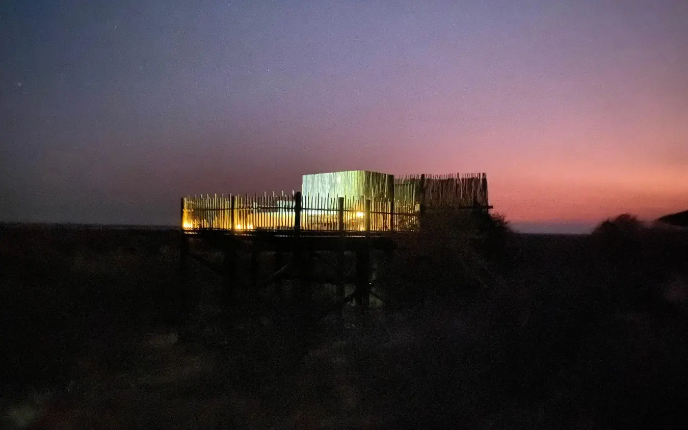 Illuminated lodge structure at dusk with pink sunset sky, Tau Pan Camp, Central Kalahari, Botswana