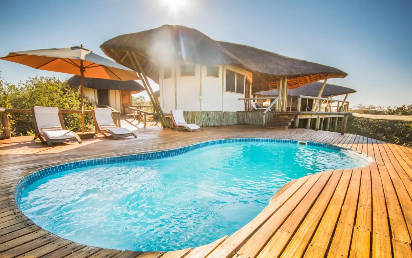 Swimming pool with wooden deck and thatched lodge buildings, Tau Pan Camp, Central Kalahari, Botswana