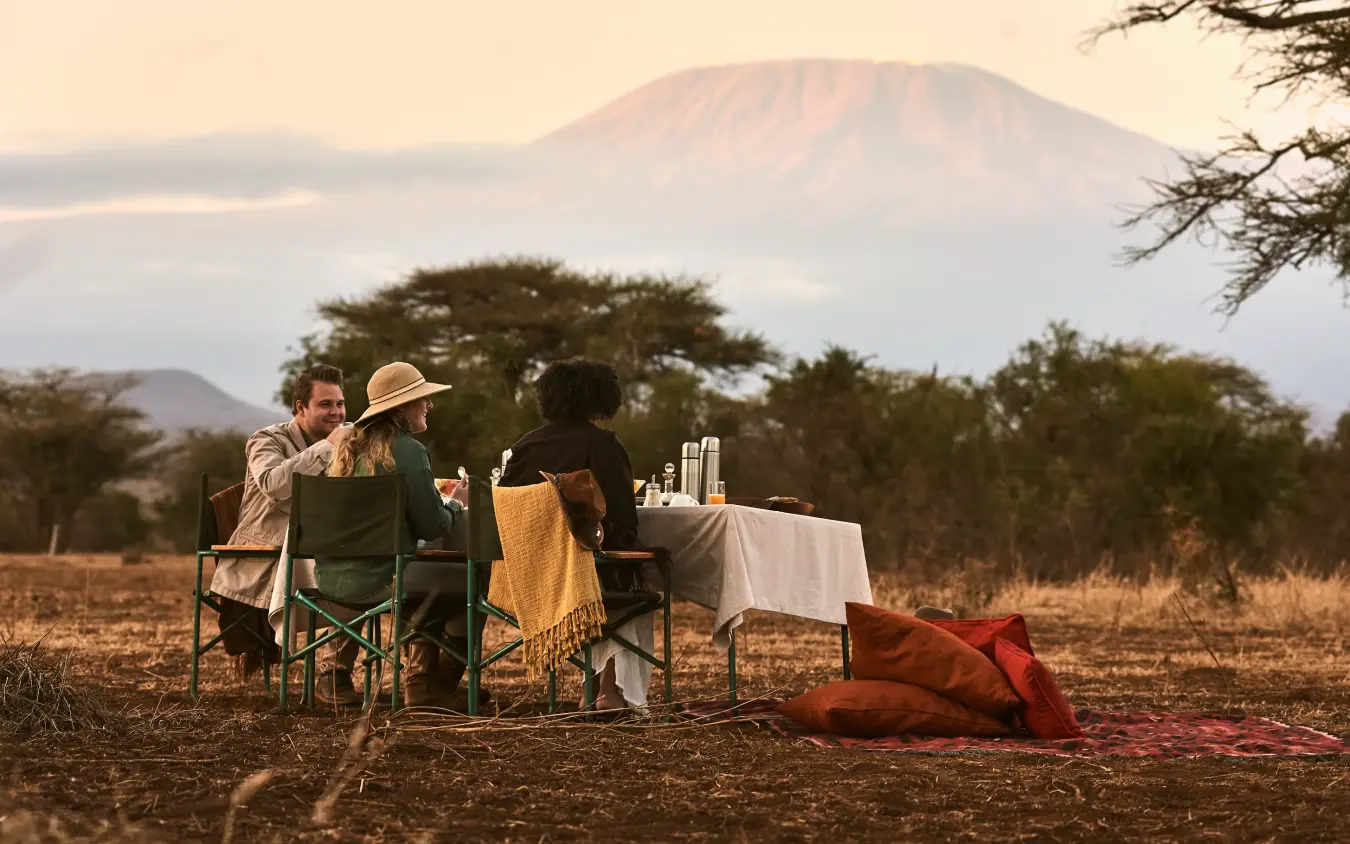 Couple dining outdoors with mountain backdrop at sunset, Tawi Lodge, Amboseli and Chyulu Hills, Kenya
