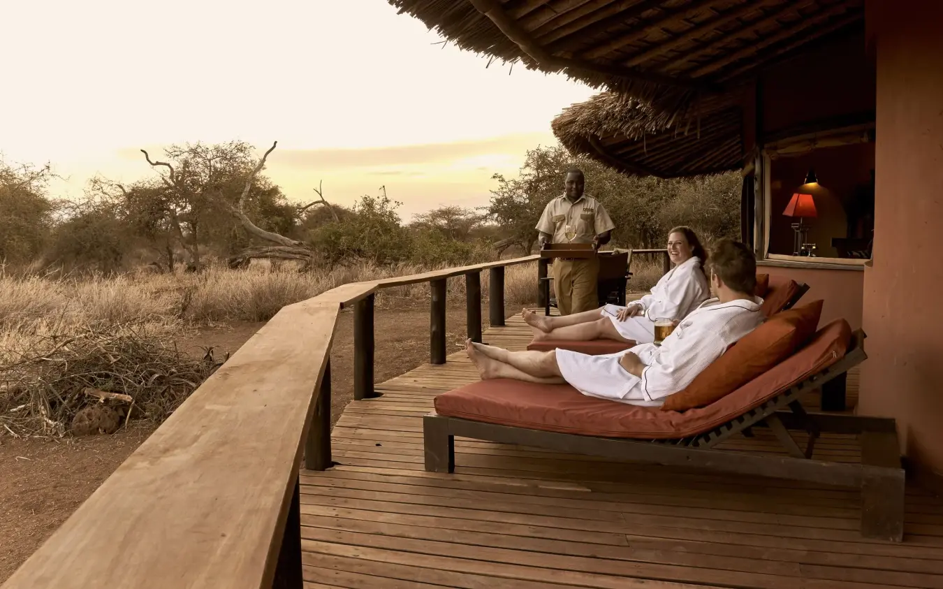 Guests relaxing on wooden deck overlooking savanna at sunset, Tawi Lodge, Amboseli and Chyulu Hills, Kenya