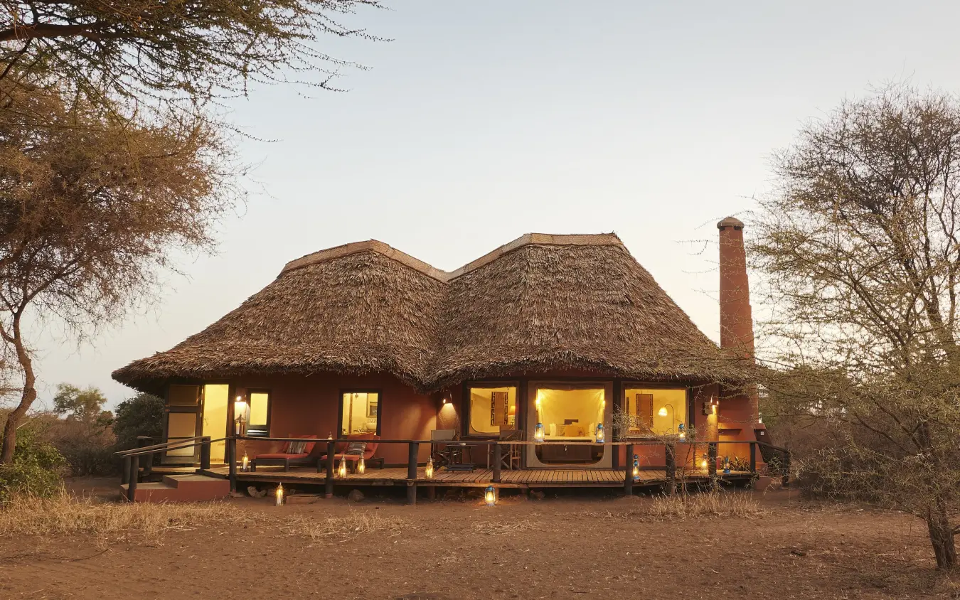 Thatched-roof lodge building at dusk with warm interior lighting, Tawi Lodge, Amboseli and Chyulu Hills, Kenya
