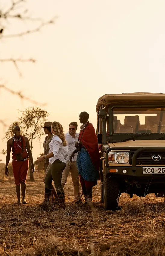 Safari vehicle with guests meeting Maasai warriors at sunset, Amboseli and Chyulu Hills, Kenya