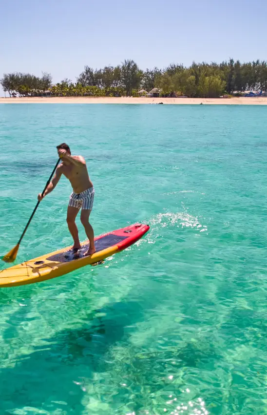 Man paddleboarding on turquoise water near sandy beach with trees, Thanda Island, Mafia Archipelago, Tanzania