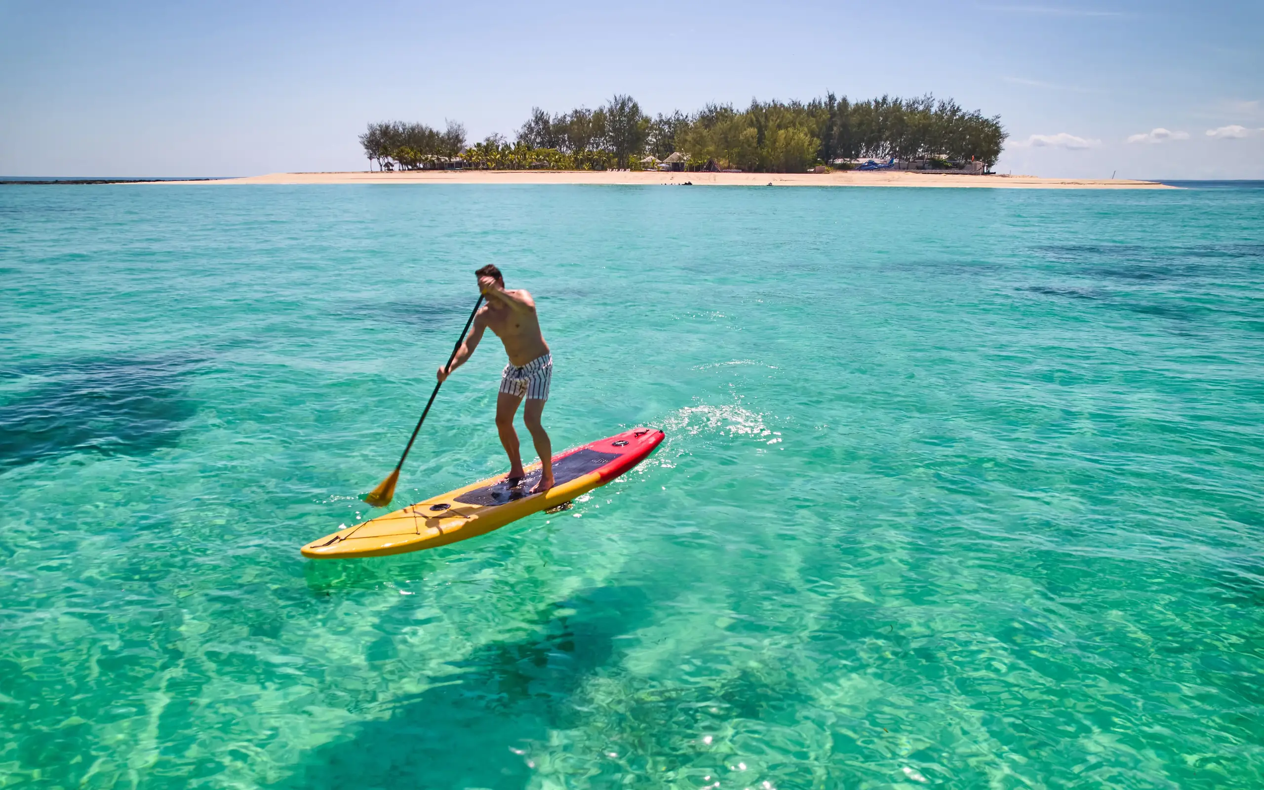 Man paddleboarding on turquoise water near tropical island, Tanzania