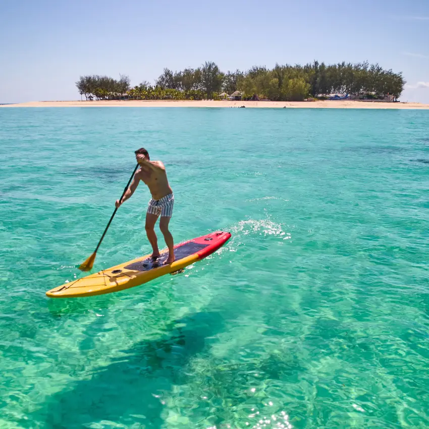 Man paddleboarding on turquoise water near tropical island, Mafia Archipelago, Tanzania