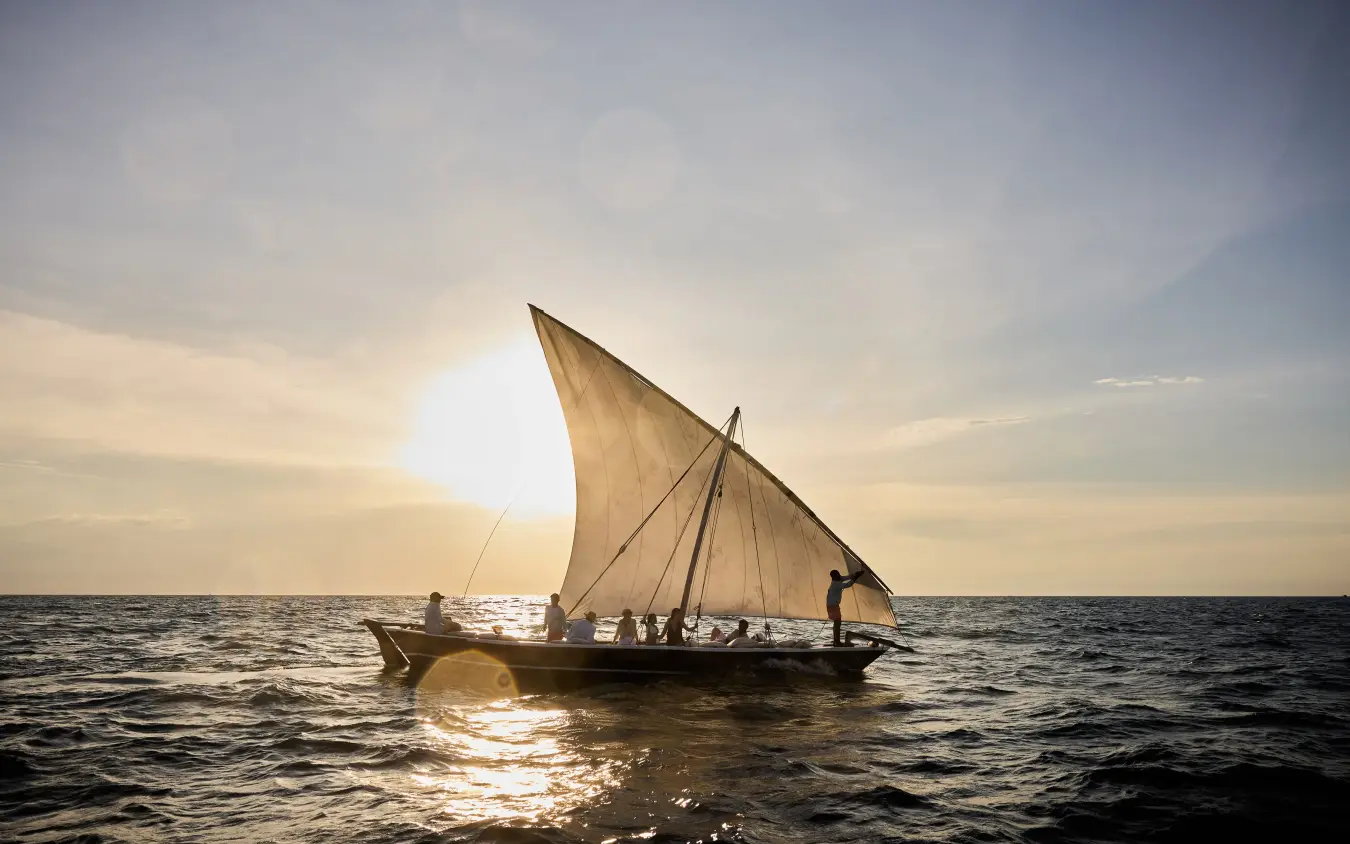 Traditional wooden sailing dhow with passengers on open ocean at sunset, Thanda Island, Mafia Archipelago, Tanzania