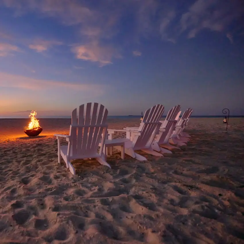 Adirondack chairs arranged on beach at sunset with bonfire, Mafia Archipelago, Tanzania
