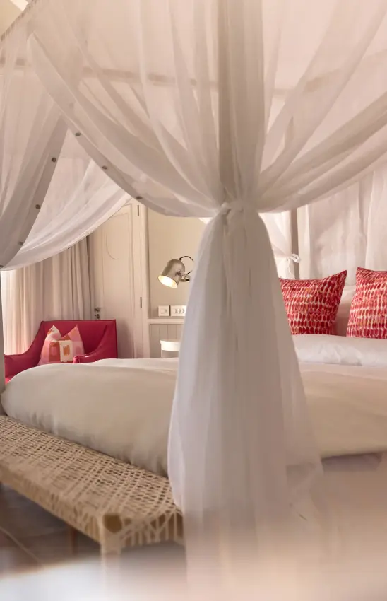 Luxury canopy bed with sheer white drapes and red patterned pillows in bedroom, Thanda Island, Mafia Archipelago, Tanzania