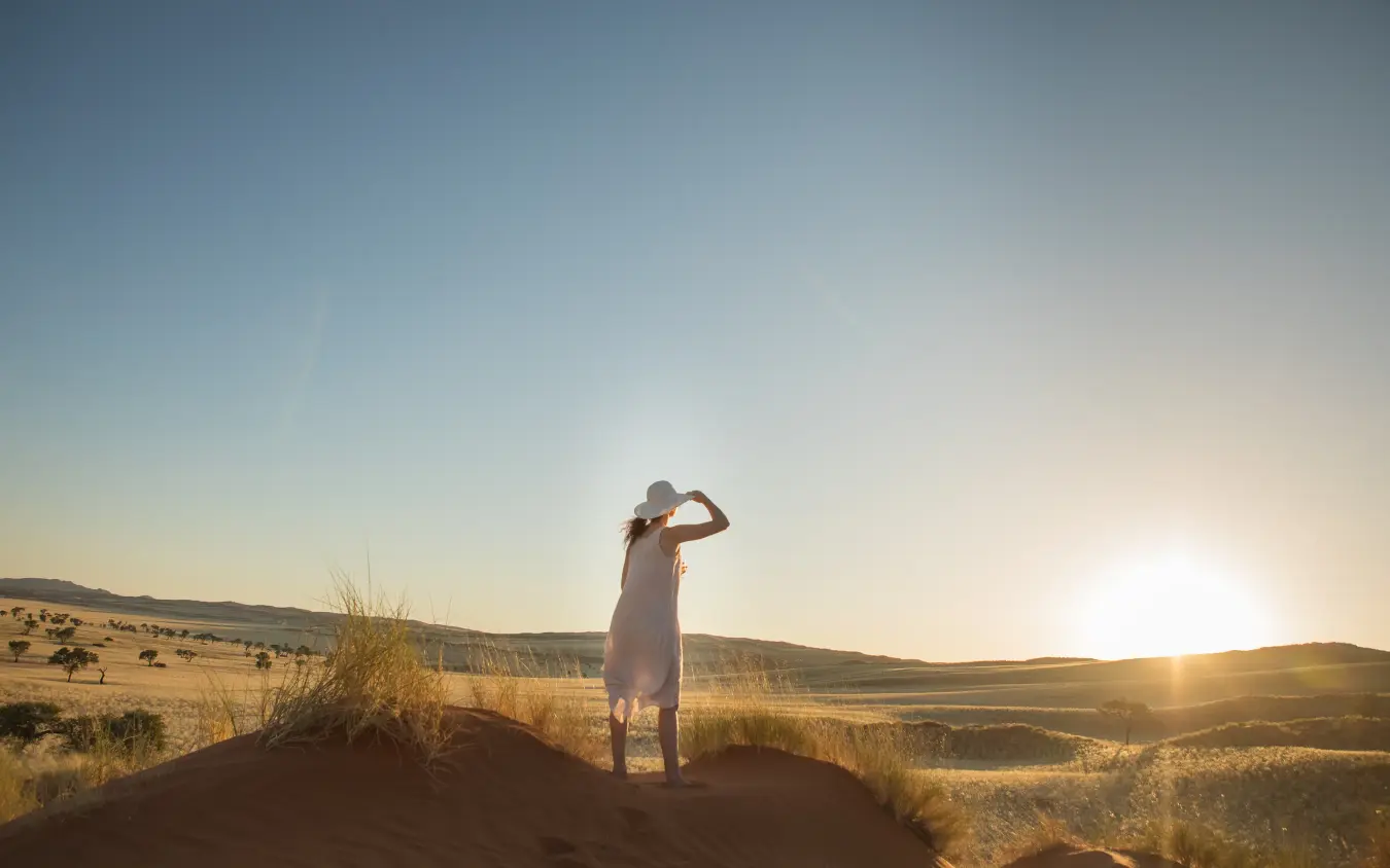 Woman in white dress standing on dune at sunset in arid landscape, The Desert Grace, Sossusvlei, Namibia