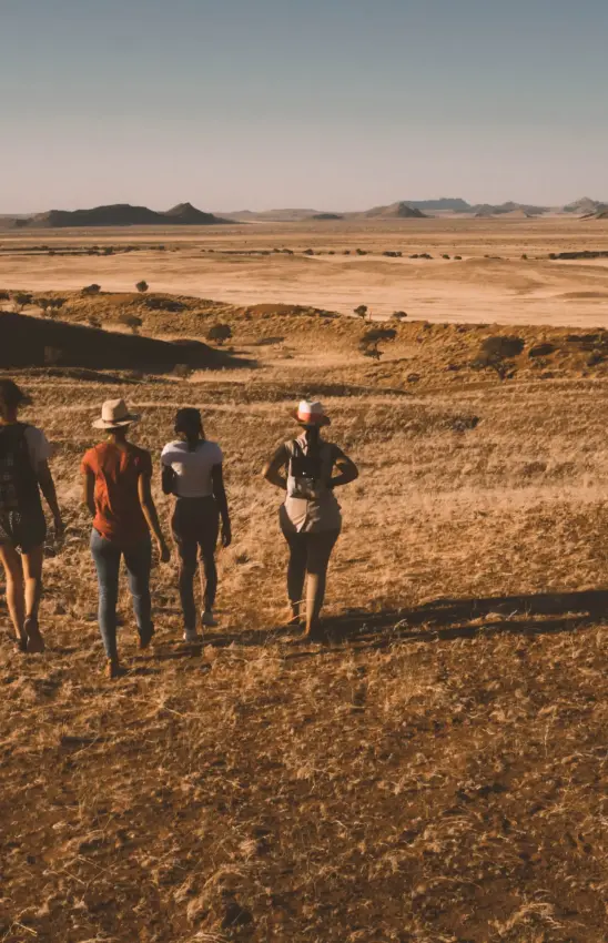 Group of hikers walking across arid desert landscape at golden hour, The Desert Grace, Sossusvlei, Namibia