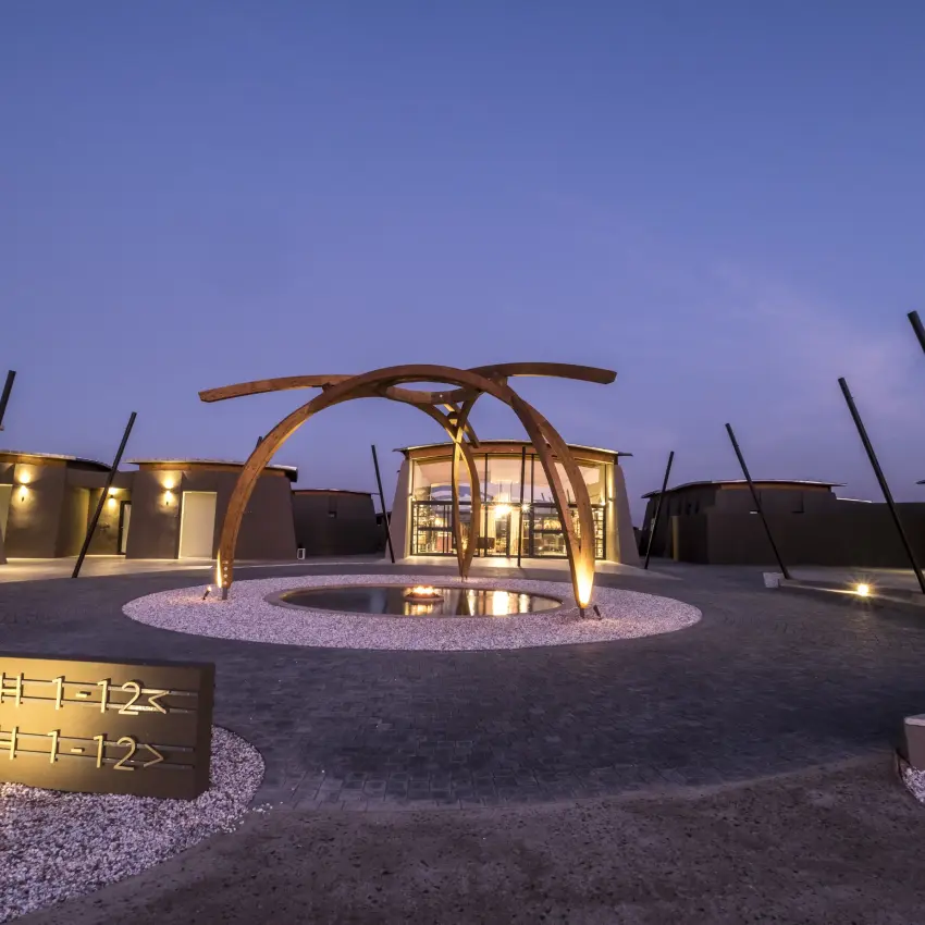 Luxury lodge pavilions with wooden arches arranged around central courtyard at dusk, The Desert Grace, Sossusvlei, Namibia