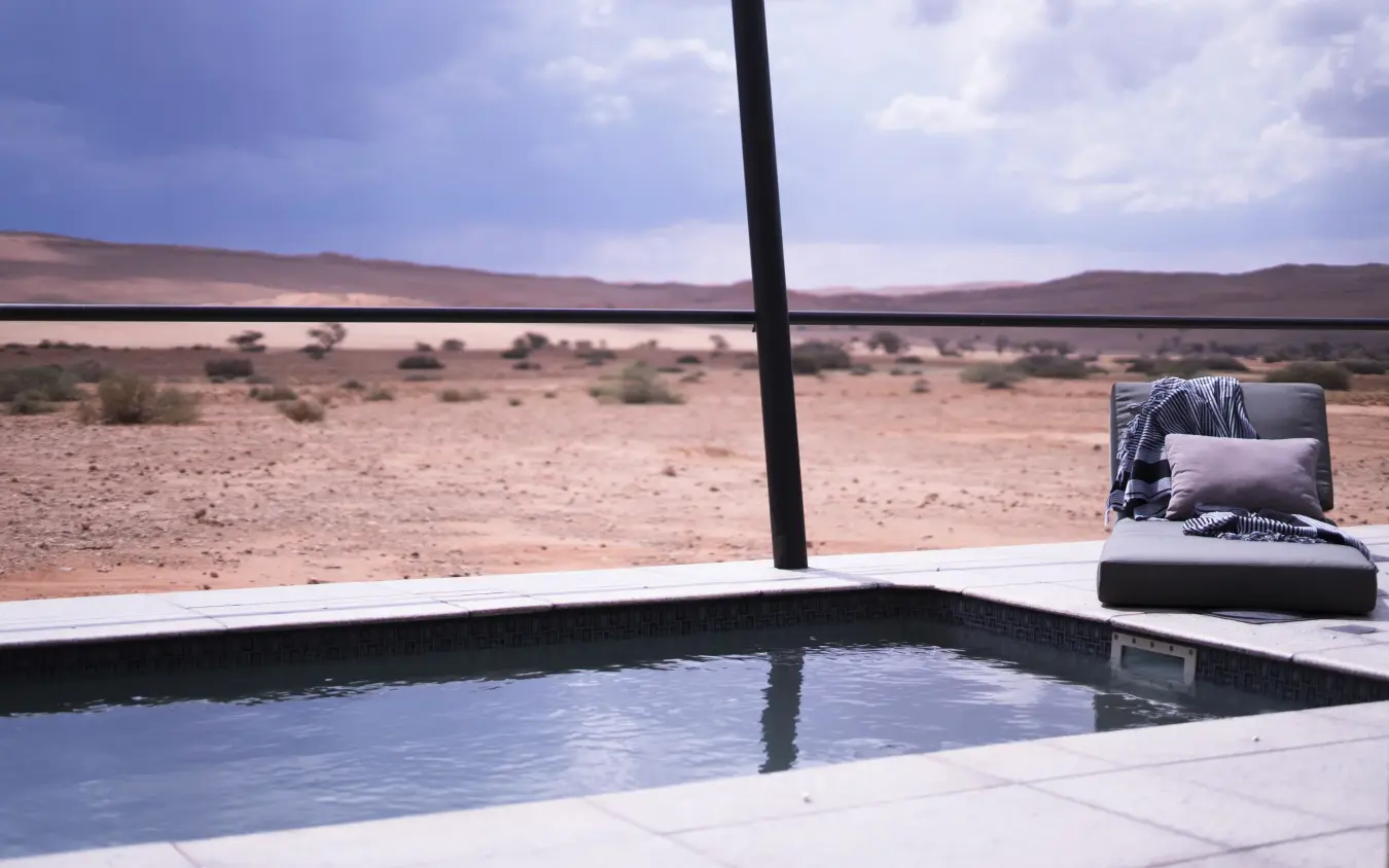 Infinity pool overlooking arid desert landscape with distant water, The Desert Grace, Sossusvlei, Namibia