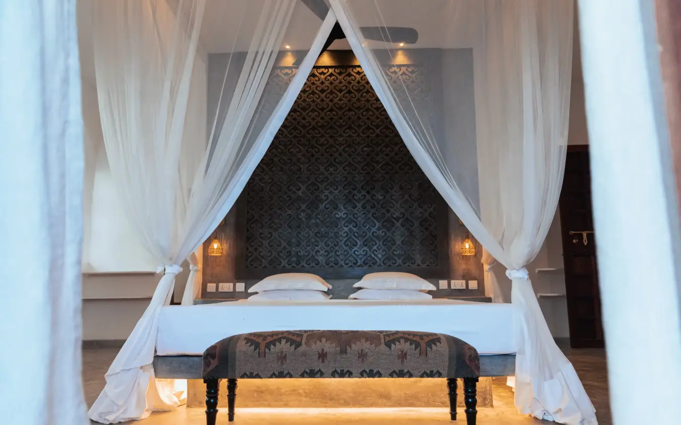 Canopy bed with white curtains and decorative bench, The Fort, Lamu Archipelago, Kenya