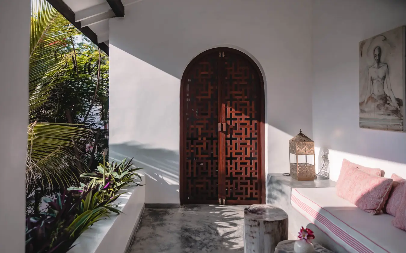 Bedroom interior with arched wooden door and garden view, The Fort, Lamu Archipelago, Kenya