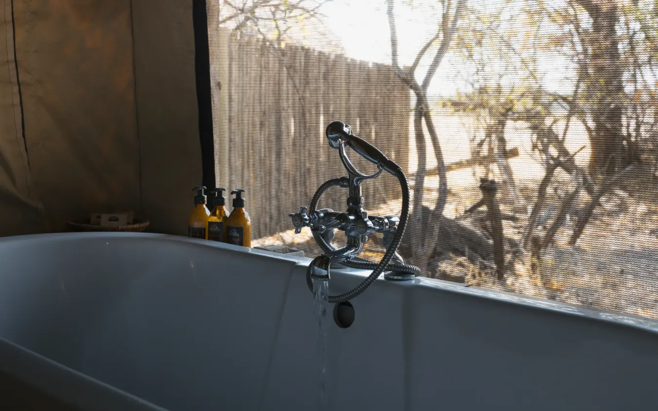 Freestanding bathtub with black faucet overlooking savanna landscape through window, The Hide, Hwange National Park, Zimbabwe