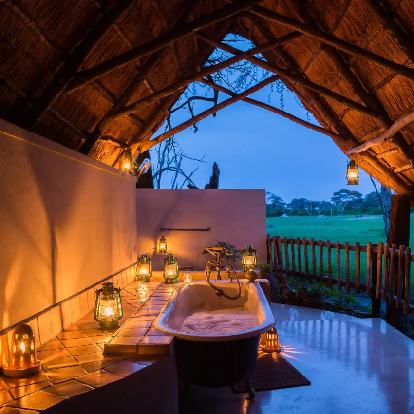 Outdoor bathroom with freestanding tub overlooking grassland at dusk, The Hide, Hwange National Park, Zimbabwe