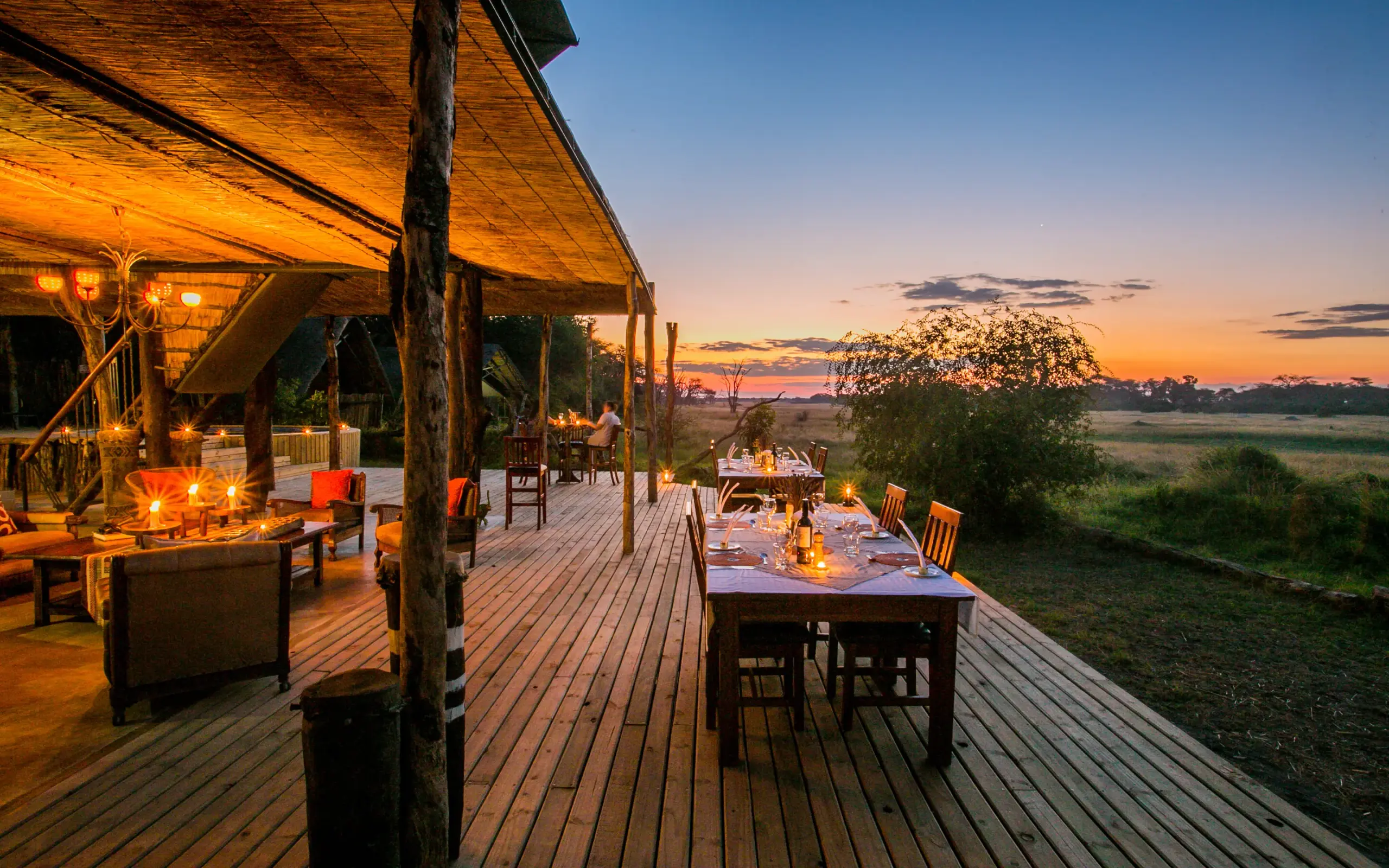 Outdoor dining deck with fire pit at sunset overlooking savanna landscape, The Hide, Hwange National Park, Zimbabwe