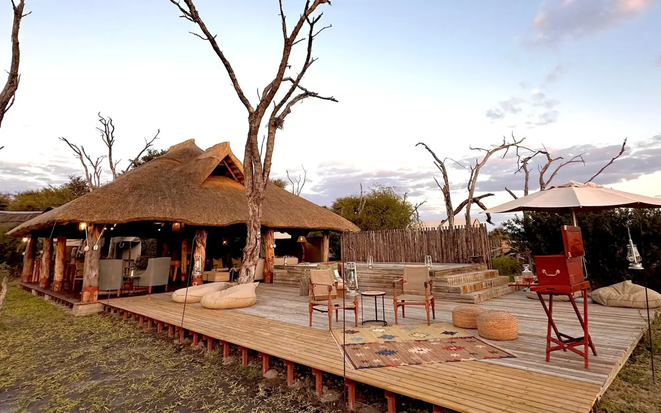 Thatched lodge with wooden deck and bare trees at dusk, The Hide, Hwange National Park, Zimbabwe