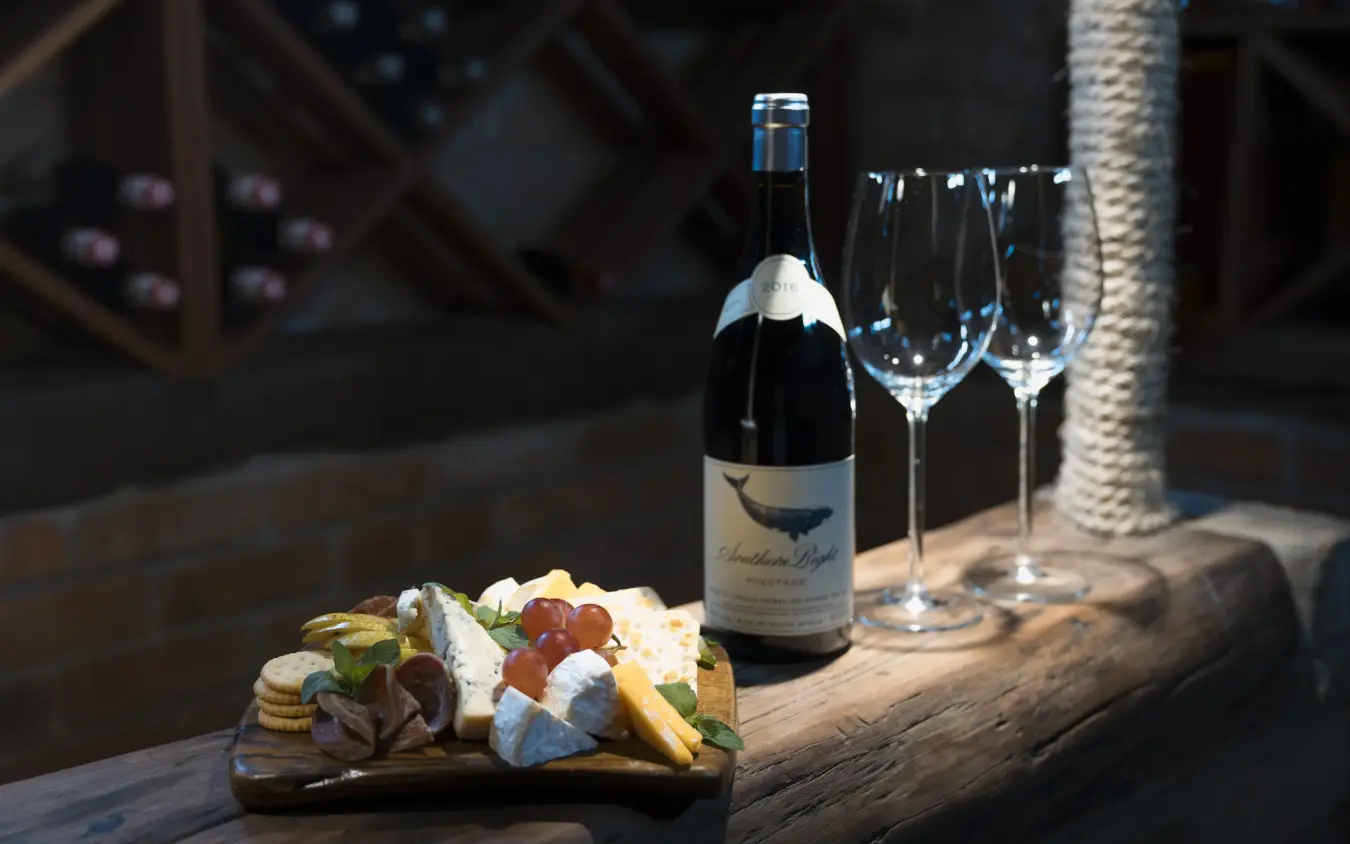 Wine bottle and charcuterie board on wooden table with palm tree, The Hide, Hwange National Park, Zimbabwe