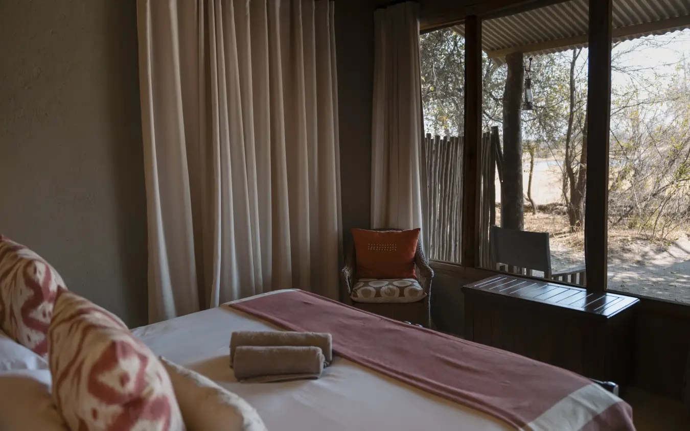 Luxury bedroom with floor-to-ceiling windows overlooking bushland landscape, The Hide, Hwange National Park, Zimbabwe