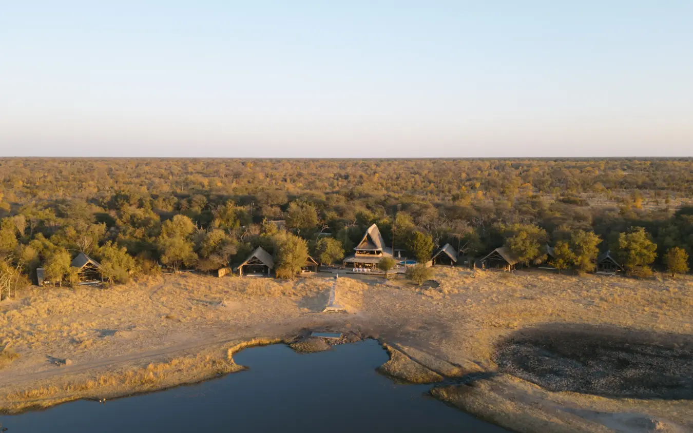 Luxury lodge with thatched roof beside waterhole at golden hour, The Hide, Hwange National Park, Zimbabwe