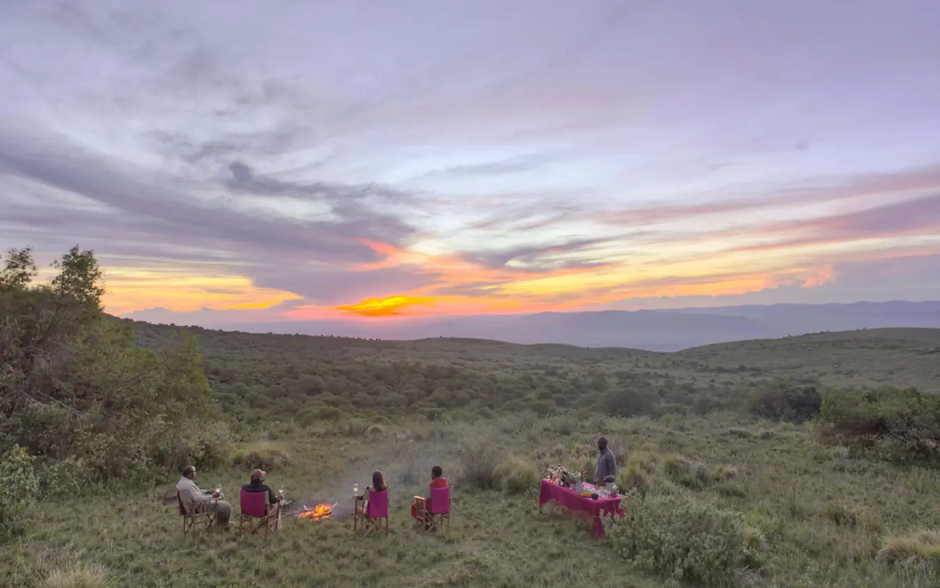 Group dining under sunset sky in savanna landscape, The Highlands, Ngorongoro Crater, Tanzania