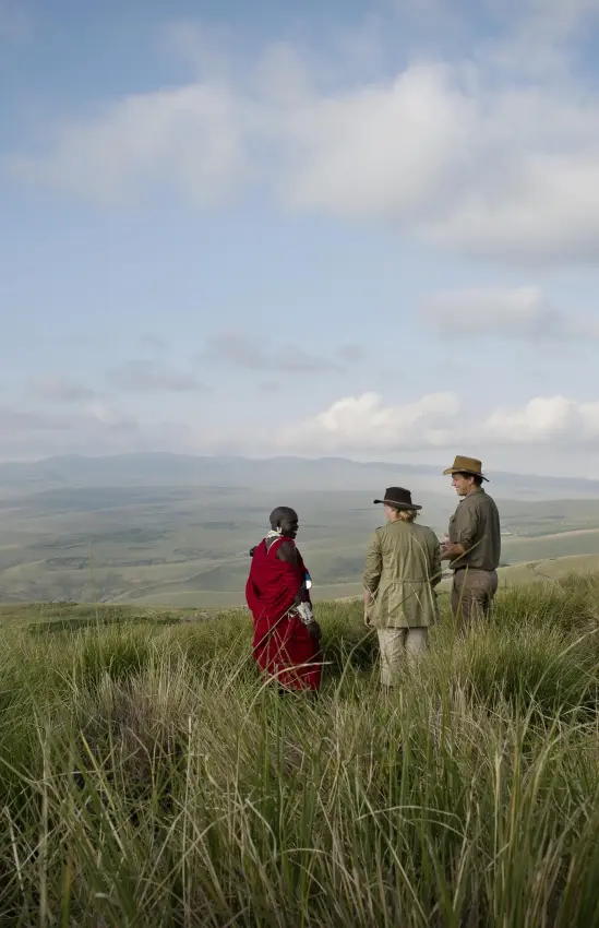 Three people hiking through grassland with mountain views, The Highlands, Ngorongoro Crater, Tanzania